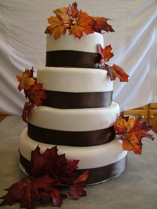 a simple white fall wedding cake with chocolate brown ribbons and dried leaf decor