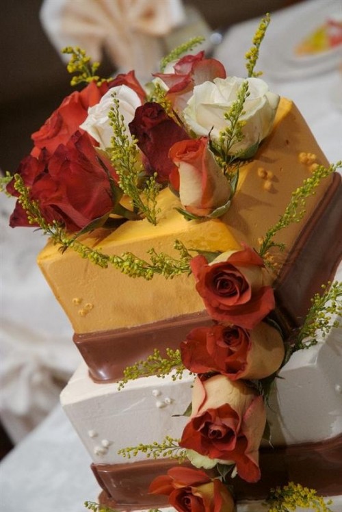 a square white and orange wedding cake with chocolate ribbons and greenery and bold fall blooms