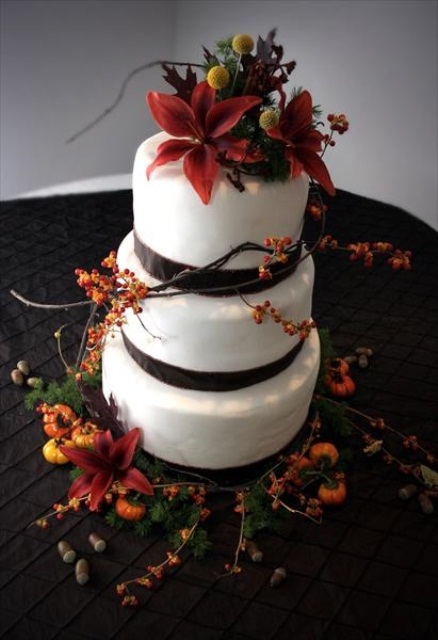 a fall wedding cake decorated with brown ribbons and bold fresh fall blooms and berries