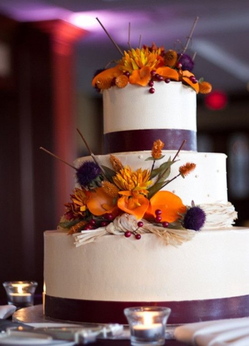 a sleek white wedding cake with purple ribbons and bright fresh fall blooms and twigs