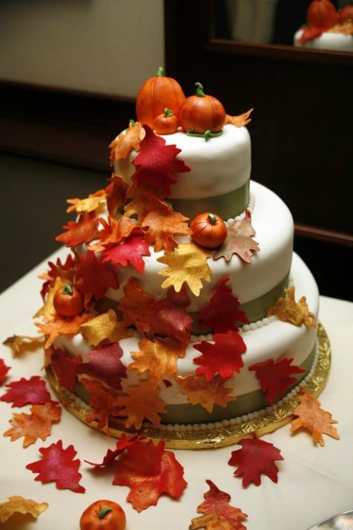 a gorgeous fall wedding cake with green ribbons and sugar leaves and pumpkins