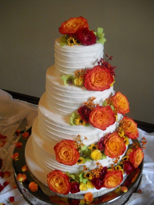 a textural white buttercream wedding cake decorated with greenery and bright fall blooms