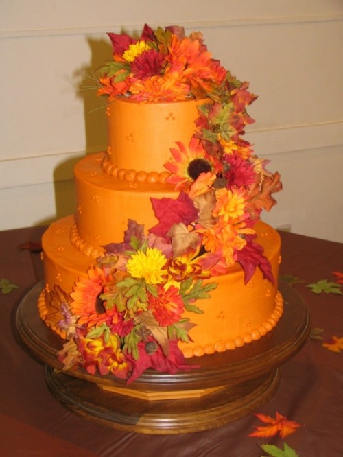 an orange wedding cake decorated with sugar leaves and blooms is a colorful idea for a fall wedding