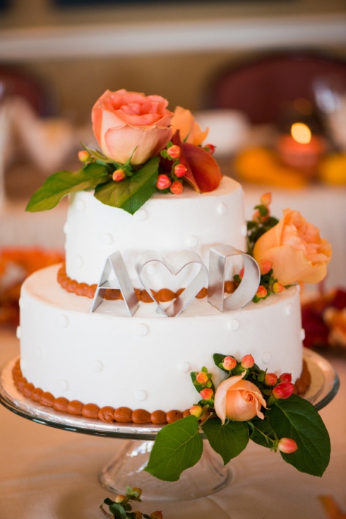 a white patterned fall wedding cake topped with fresh fall blooms and berries and monograms will always work