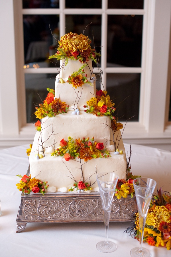 A white square wedding cake decorated with twigs, berries and bright fall blooms looks pretty natural