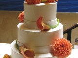 a white fall wedding cake decorated with orange blooms looks and feels fall-like