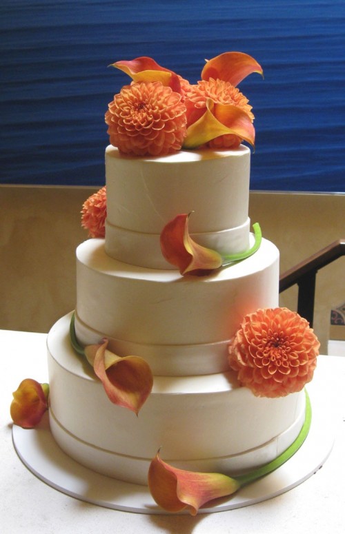 a white fall wedding cake decorated with orange blooms looks and feels fall-like