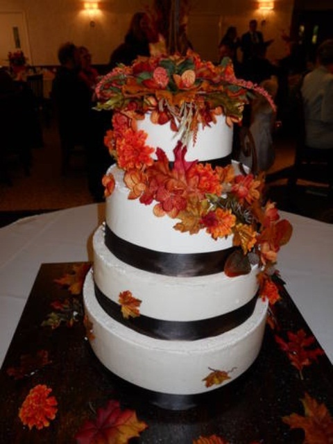 a dramatic white wedidng cake decorated with dark ribbons and bright fall-colored blooms and leaves