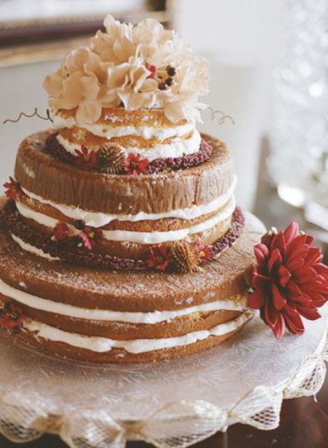 a naked wedding cake with bright fall blooms, acorns and lush neutral flowers on the top