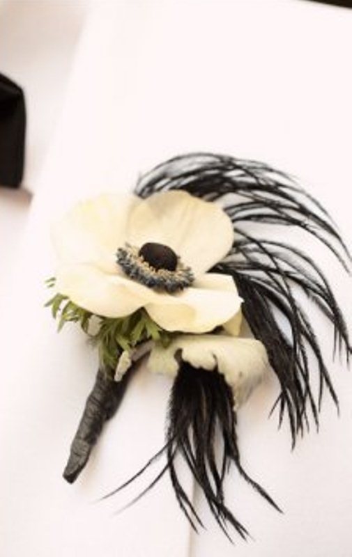 A white bloom boutonniere with black feathers and greenery