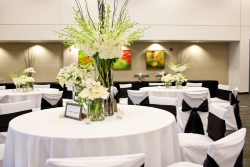 white tablecloths, white chair covers and blakc bows for a formal wedding hall