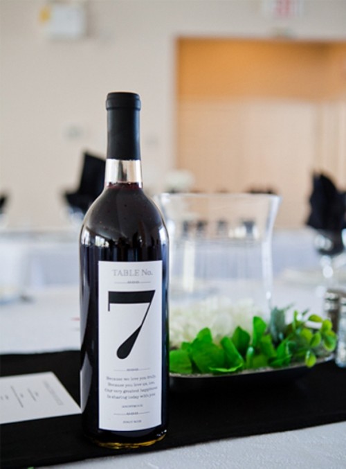 a bottle with black wine and a table number plus fresh greenery