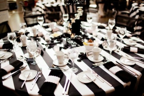 a stylish black and white wedding tablescape with a striped tablecloth, black and white napkins and a centerpiece