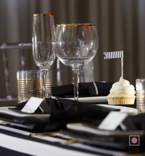 a simple place setting with white chargers, black napkins and gilded touches for more chic