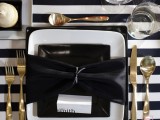a stylish wedding place setting with a black and white tablecloth, gold cutlery and black and white plates