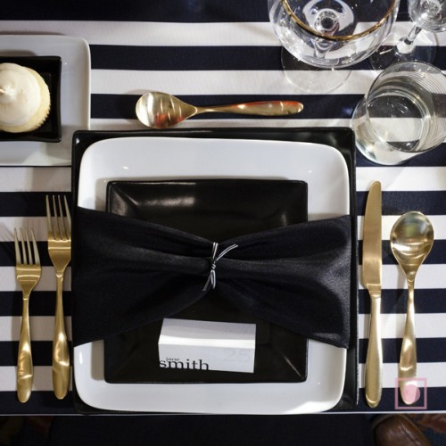a stylish wedding place setting with a black and white tablecloth, gold cutlery and black and white plates