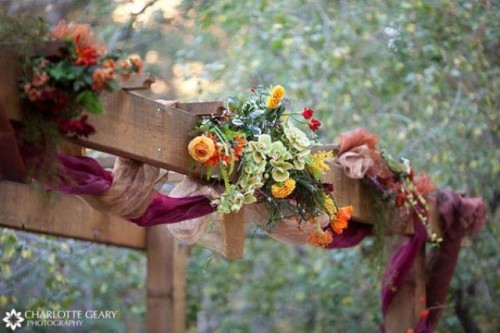 a fall wedding arch decorated with burgundy curtains and green and bright blooms on top