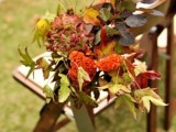 decorate the aisle chairs with bold fall foliage and blooms for your outdoor wedding ceremony