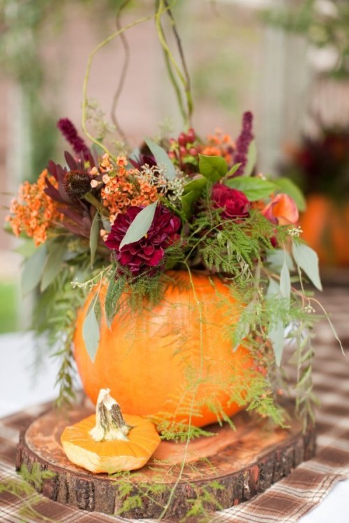 a rustic fall wedding centerpiece with a wood slice, a pumpkin with a bright fall floral arrangement and greenery
