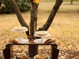 a dessert table placed under a table and a wooden basket with pinecones and apples