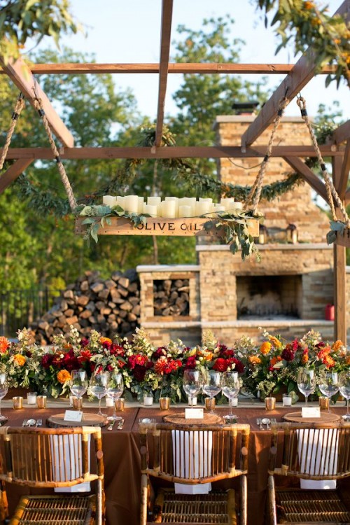 a chic rustic fall reception table with a box with candles, a bright floral table runner and rattan chairs