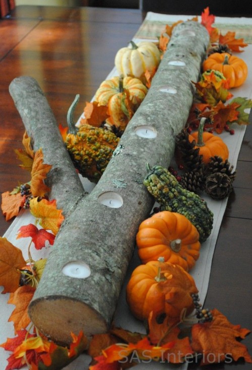 a fall wedding centerpiece with a log with candles and bright fall leaves, gourds and pumpkins