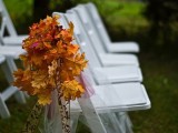 simple white chairs decorated with bright fall leaves and tulle for an outdoor wedding ceremony
