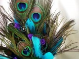 a wedding centerpiece compsoed of peacock and turquoise feathers in a purple vase