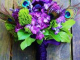 a purple and green wedding bouquet with peacock feathers and a purple wrap