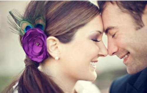 a wedding hairpiece made of a purple fabric flower and peacock feathers