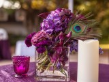 a purple floral wedding centerpiece accented with a peacock feather and candles around
