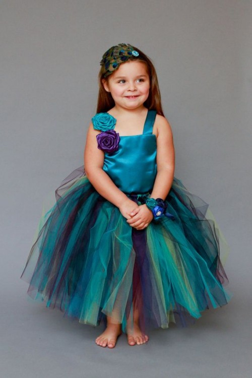 a bright teal flower girl dress with purple accents and a fun peacock feather hairpiece