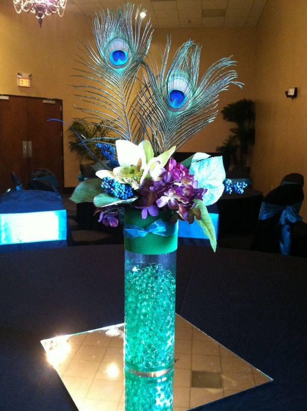 A turquoise wedding centerpiece with purple touches and peacock feathers