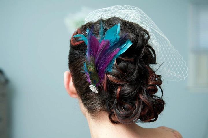 A bright wedding hairpiece of turquoise, purple and peacock feathers plus a cage veil on the other side
