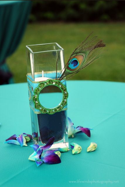 a vase with a candle, a mirror and a peacock feather for a wedding centerpiece