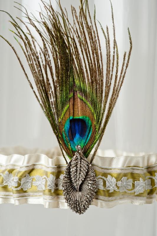 A wedding garter with a peacock feather and a vintage brooch is a unique accessory