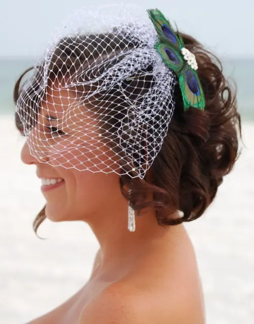 a birdcage veil with a vintage brooch and a peacock feather attached