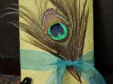 a wedding card accented with a peacock feather and a blue ribbon