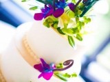 a wedding cake topped with purple blue and green blooms and peacock feathers