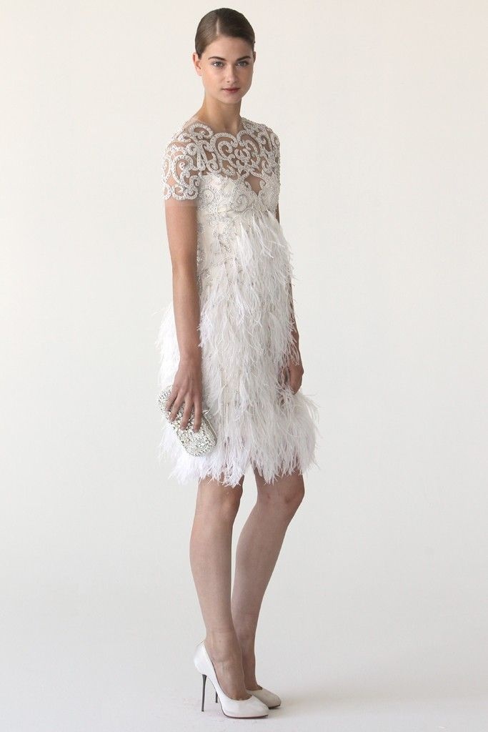 A short art deco wedding dress with an illusion embellished patterned neckline and a feathered skirt plus an embellished clutch and white shoes