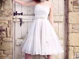 a white vintage-inspired A-line wedding dress with a pleated skirt, lace appliques and a large bow