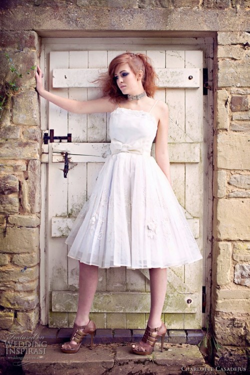 a white vintage-inspired A-line wedding dress with a pleated skirt, lace appliques and a large bow