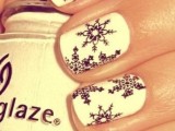 a white manicure with black snowflake stickers is a stylish and contrasting idea to make your look extra bold