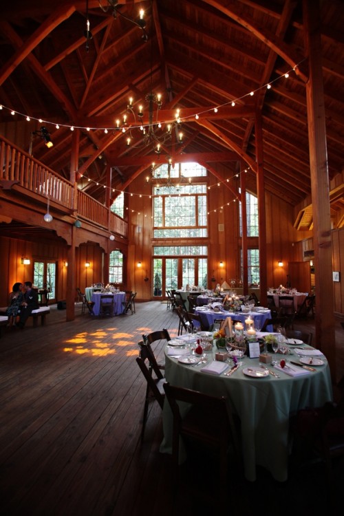 a barn wedding venue with string lights, chandeliers and sconces for a cozy and intimate atmosphere in the space