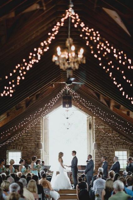 string lights paired with elegant chandeliers are amazing to light up a wedding venue, whether it's a barn or not