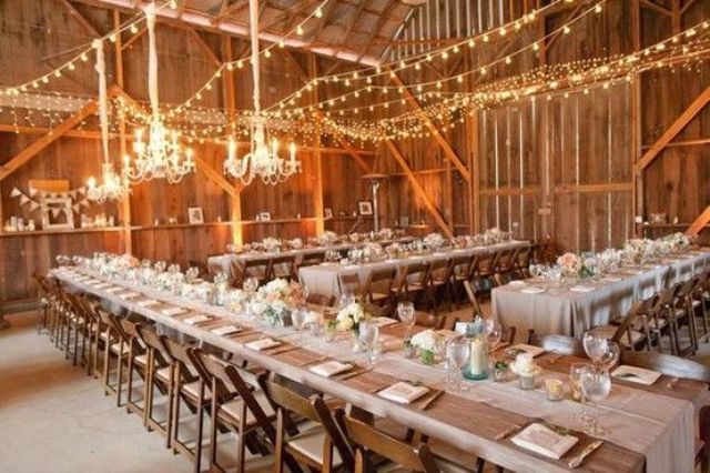 a rustic barn wedding venue with string lights paired with chandeliers is coy, welcoming and bright lit up