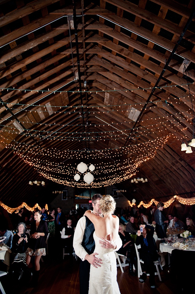 a barn wedding venue with string lights over the whole space that create an ambience and give a romantic look to the space