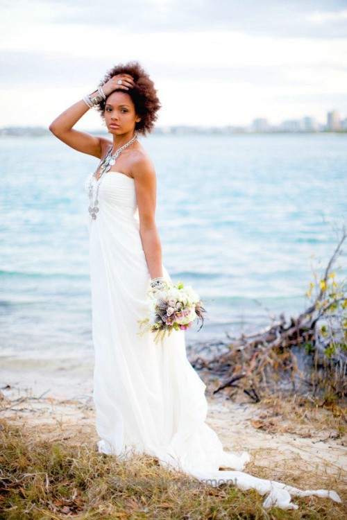 a strapless and draped maxi wedding gown with a train, layered necklaces and bracelets for a chic beach bridal look