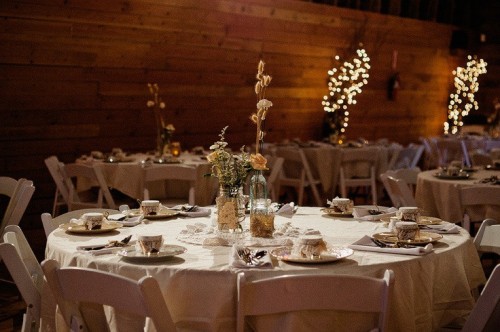 a neutral barn wedding tablescape with neutral linens, a dried bloom centerpieces and vintage porcelain and mugs