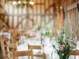 a chic neutral barn wedding tablescape with white linens, a neutral bloom wedding centerpiece in a vintage jug and simple cutlery